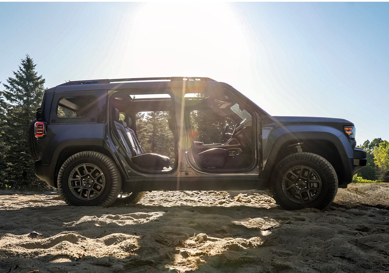 2026 Jeep Recon with open doors on a sandy terrain in sunlight, surrounded by trees.