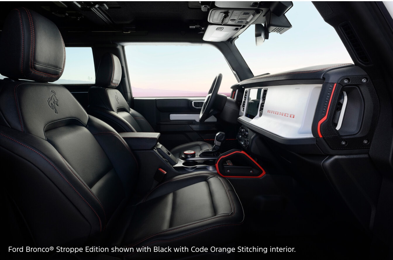 Interior cabin view of a Ford Bronco Stroppe Edition in Black with Code Orange Stitching highlighting the dashboard and front seats.
