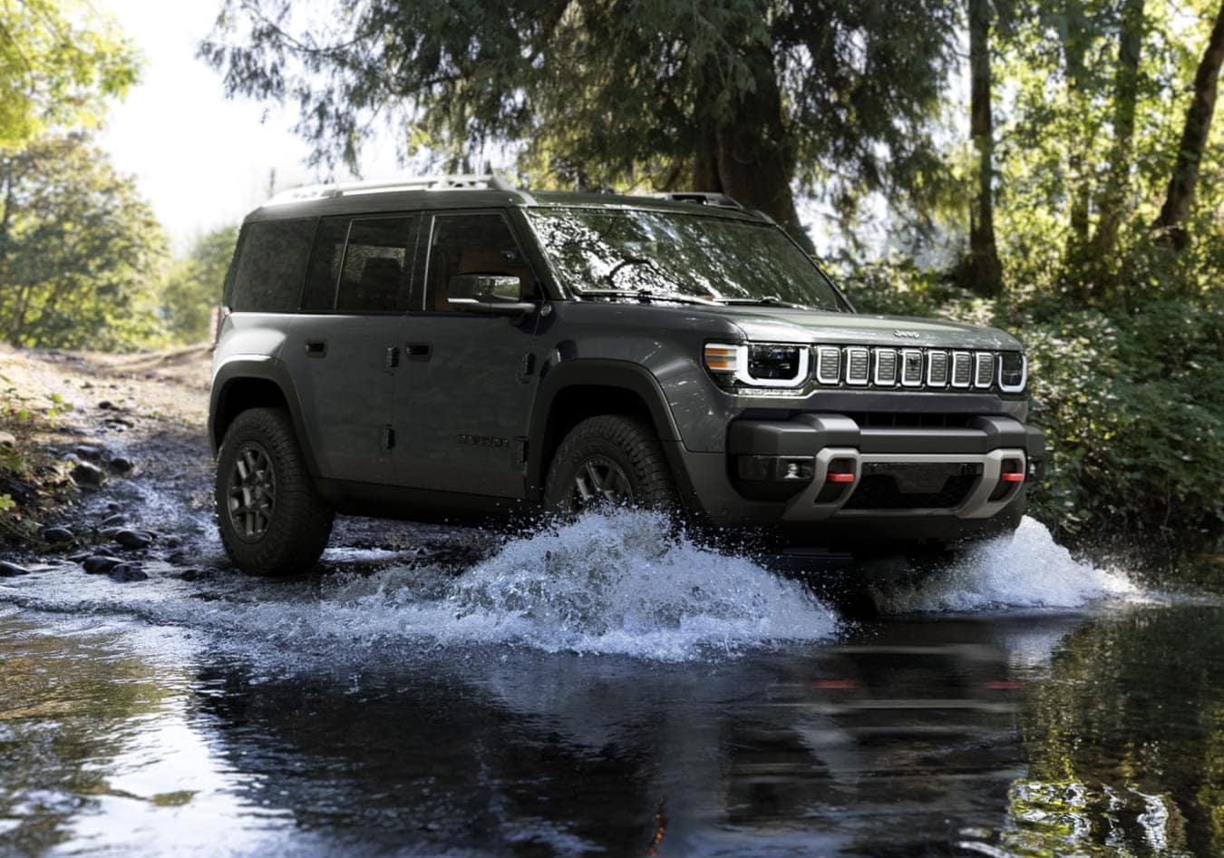 2026 Jeep Recon crosses a forest stream, splashing water. Sunlight filters through the trees, creating a sense of adventure and freedom.