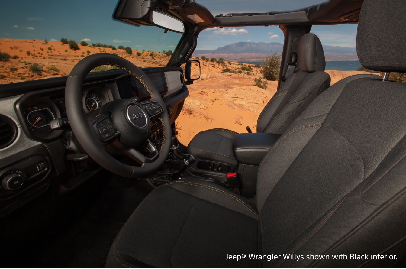 Interior cabin view of a Jeep Wrangler Willys with a Black cloth interior parked in an open-air desert landscape.