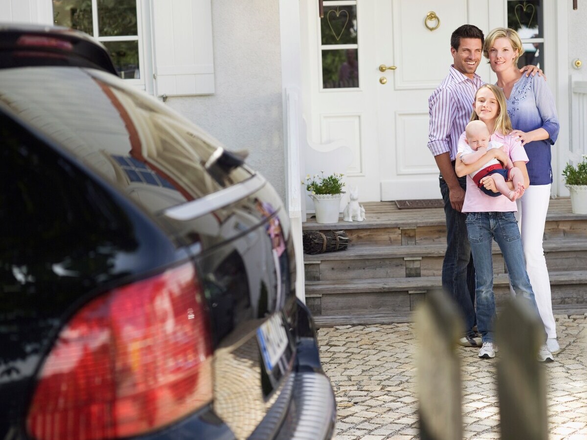Family in the front side of the house with a car at one side