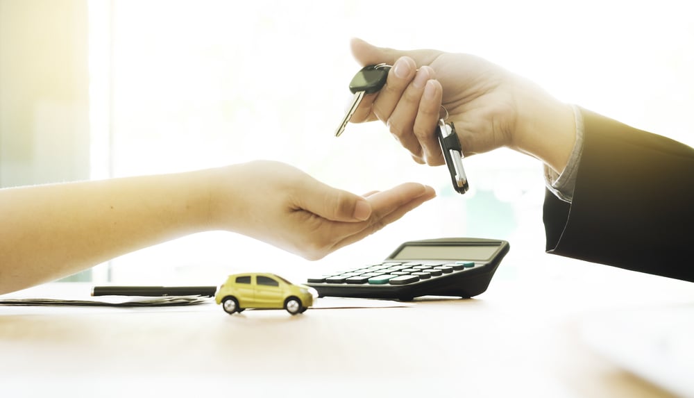 Passing car keys with calculator and toy car in the background