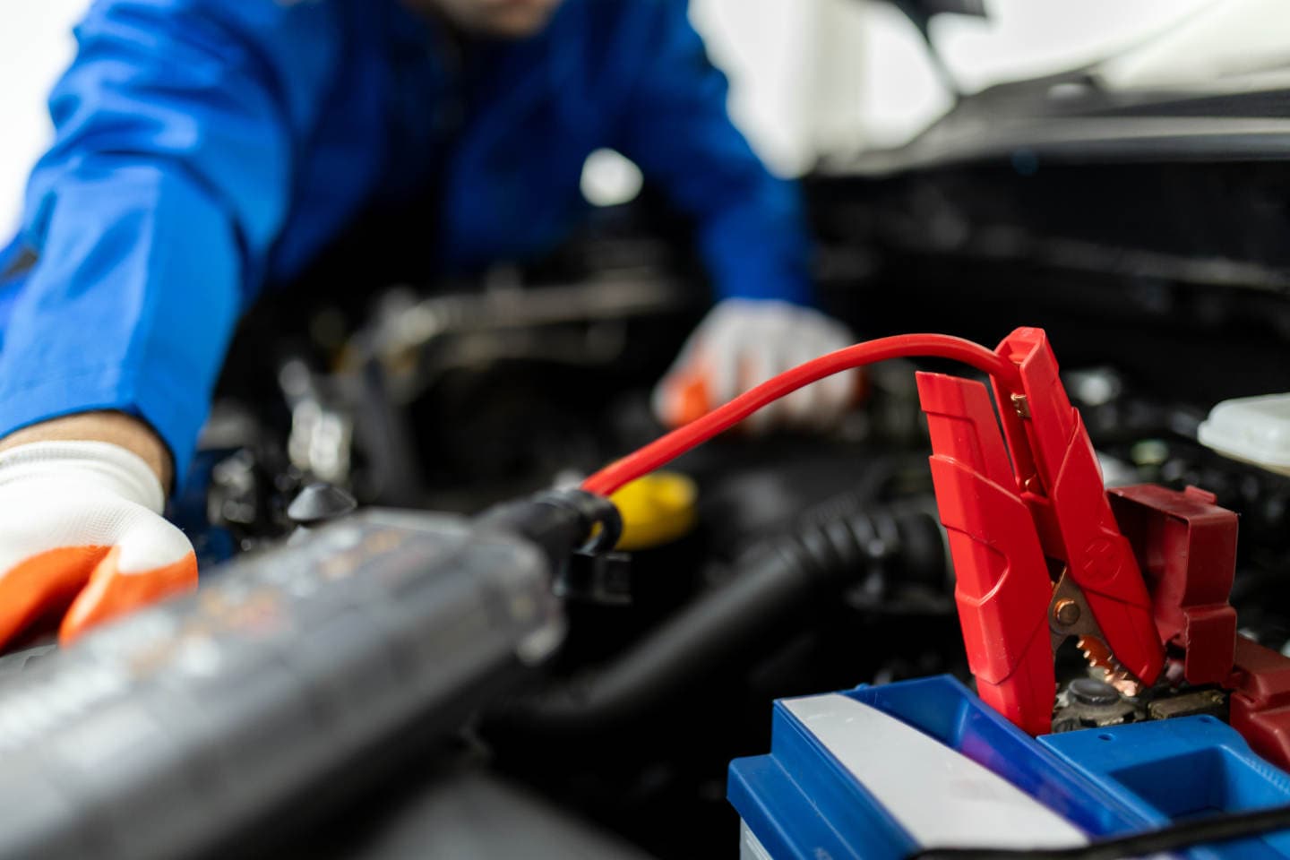 Mechanic uses a jumper cable clamp on a car battery while servicing the engine compartment