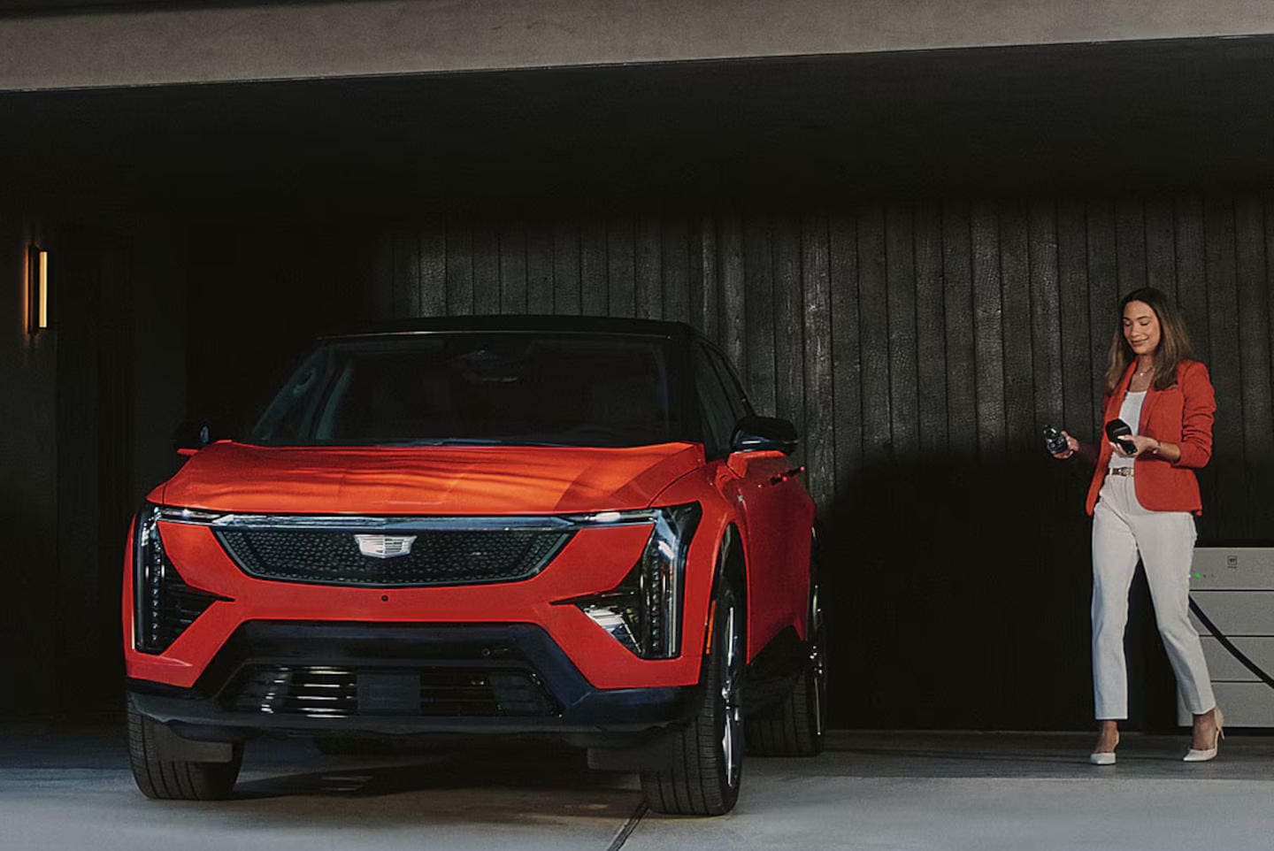 Woman preparing to charge a red 2027 Cadillac OPTIQ in a home garage