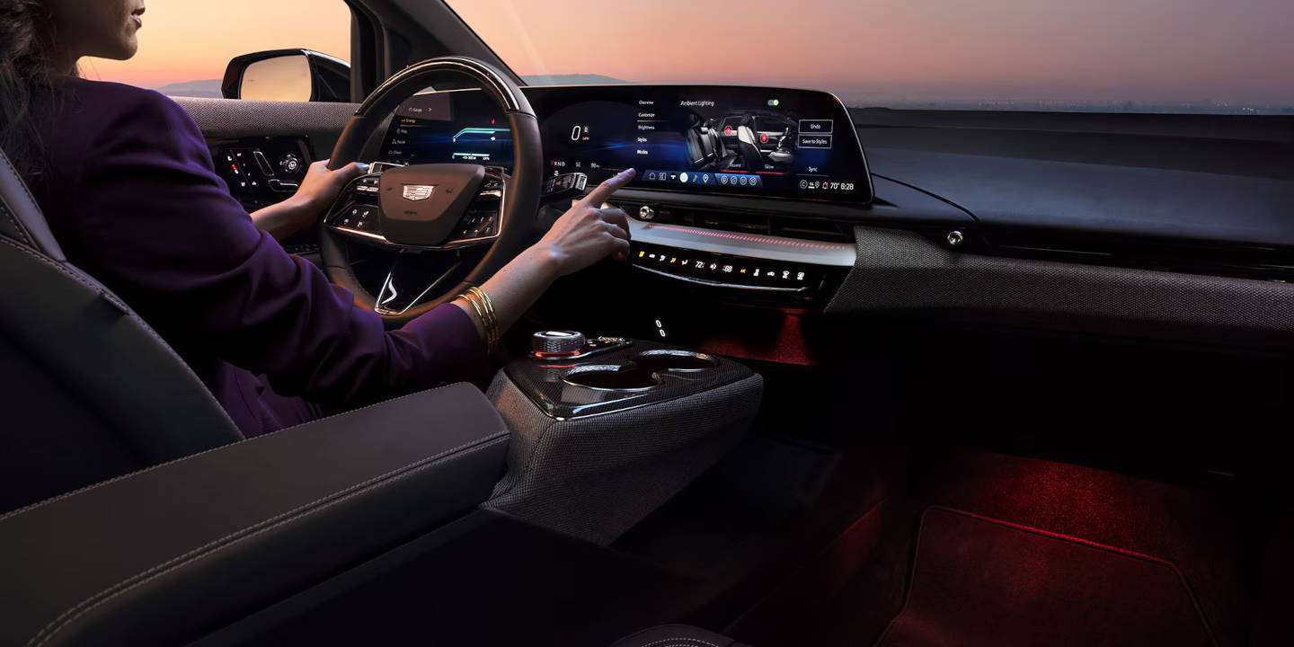 Cadillac steering wheel and dashboard with a women adjusting a setting on the dashboard