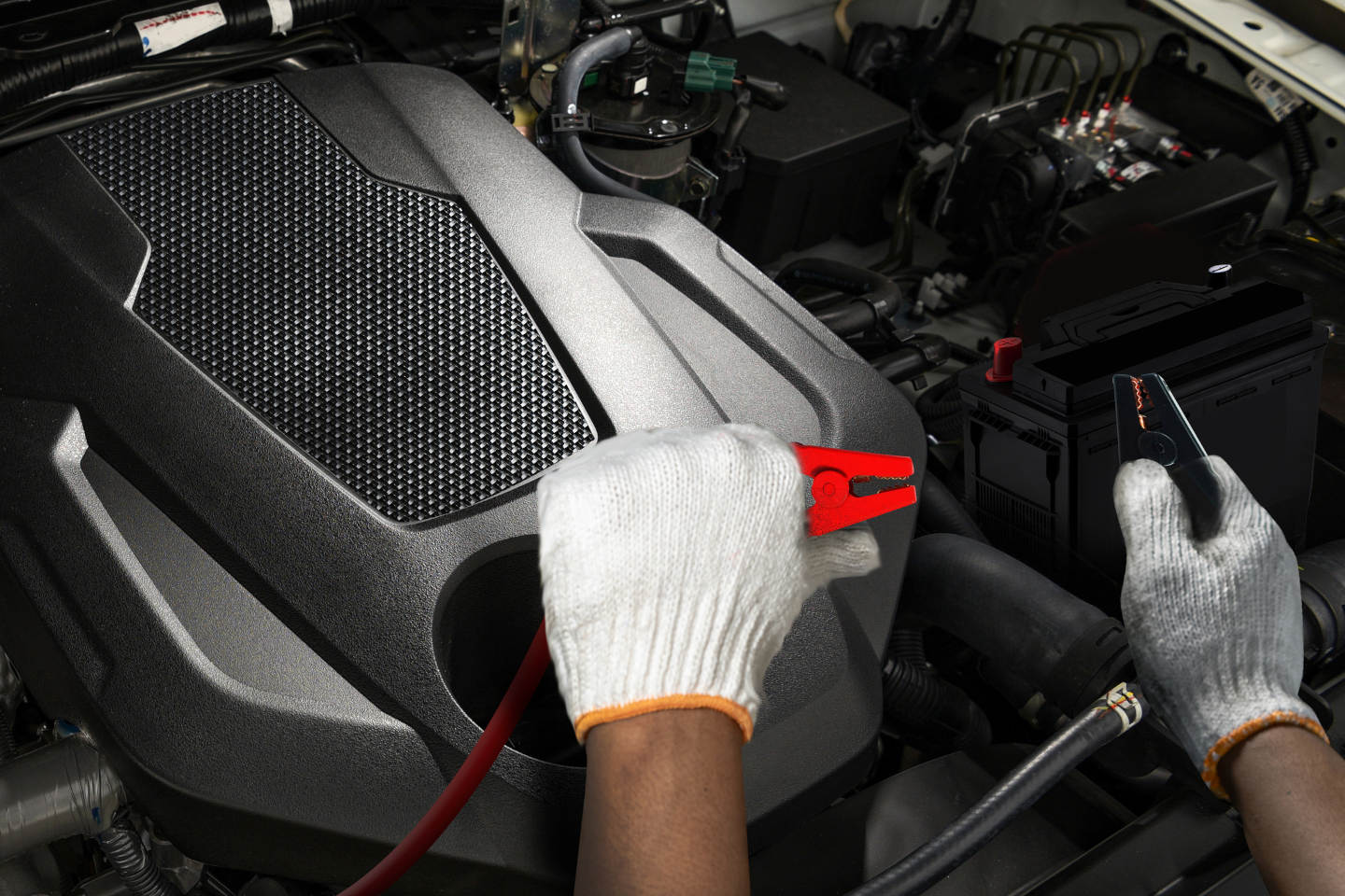 Close-up of a mechanic wearing protective gloves jump starting a car battery using jumper cables inside the engine compartment