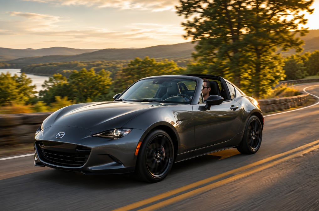 Mazda MX-5 Miata RF driving along a scenic lakeside road at sunset.