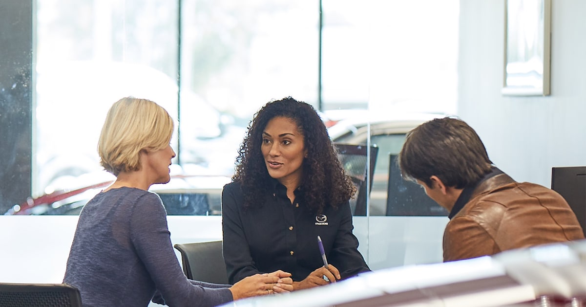  Mazda sales rep with customers in showroom.