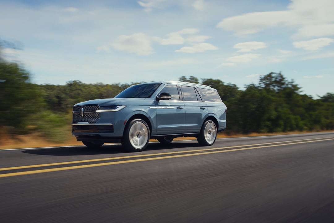 Gray Mist 2025 Lincoln Navigator Reserve drives down a two lane highway on a bright, sunny day.