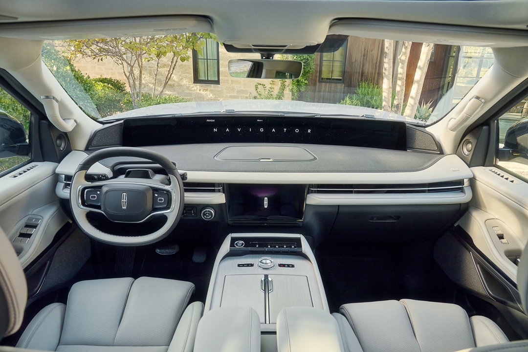 Interior shot of front row and dashboard of 2025 Lincoln Navigator Reserve with white interior. 48-inch panoramic display reads 'Navigator.'