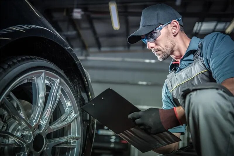 Auto Technician checking tire pressure holding a clipboard