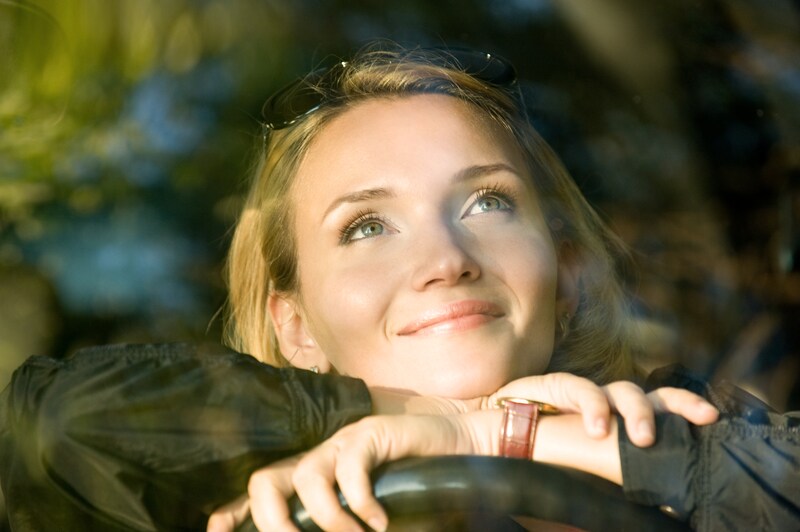 A woman leans on her steering wheel while staring into the sky