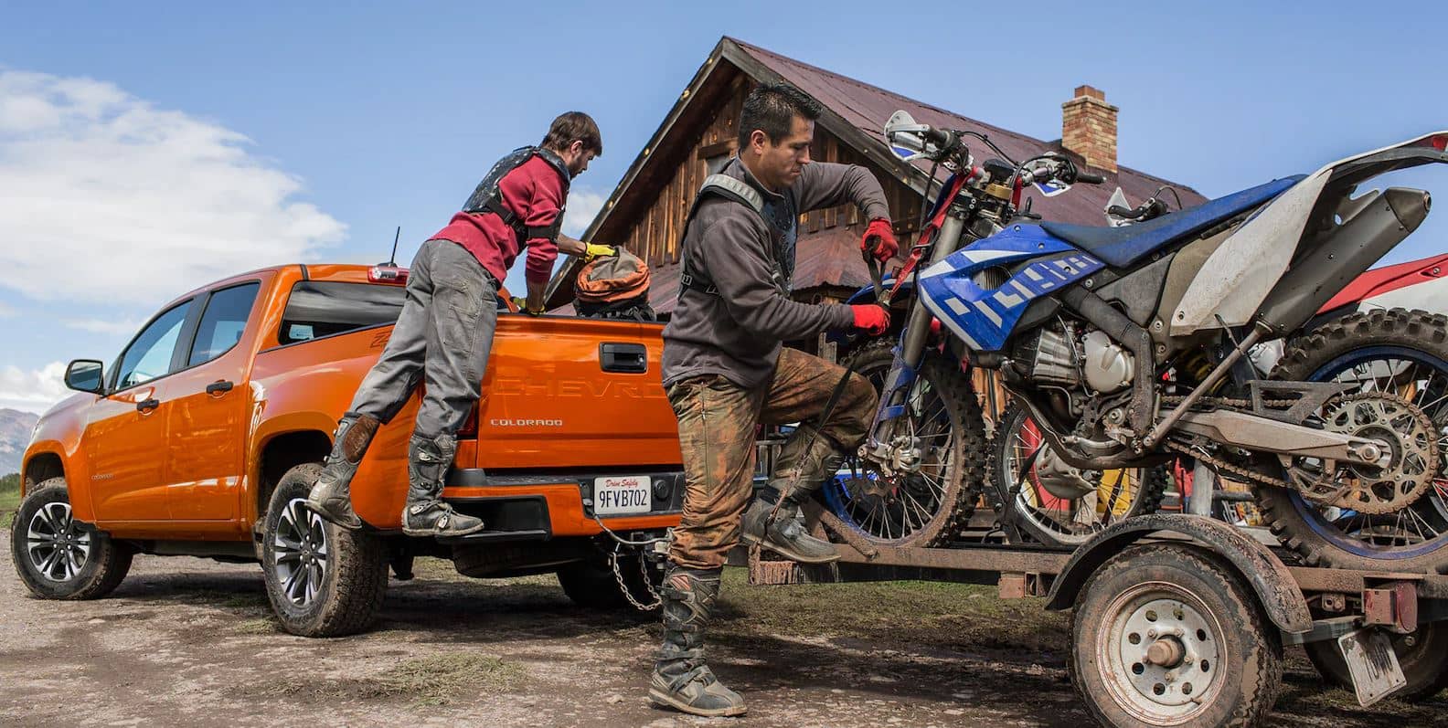 two men load 4-wheelers on a trailer attached to an orange 2023 Chevy Colorado Truck