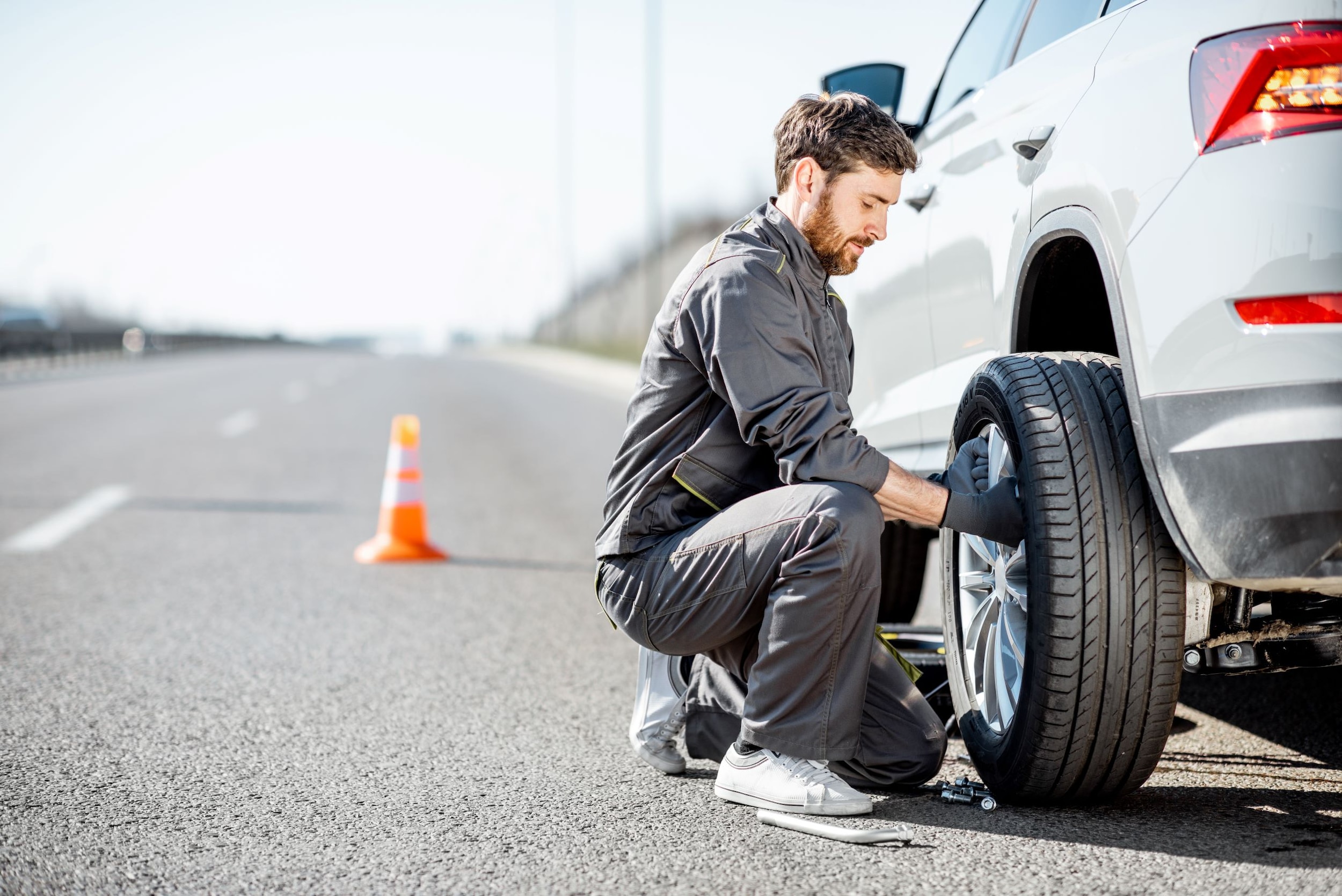 A man replacing a tire on the side of a road.