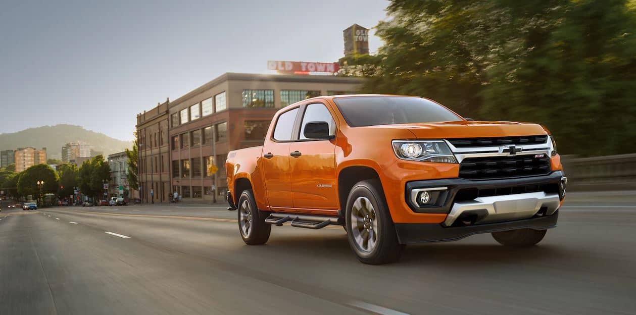 An orange 2023 Chevy Colorado driving down the road in an urban area
