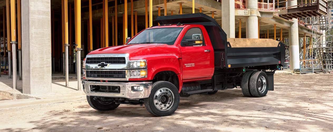 A red 2023 Chevy Silverado Work Truck has been customized with a dump truck bed and is parked at a construction site.