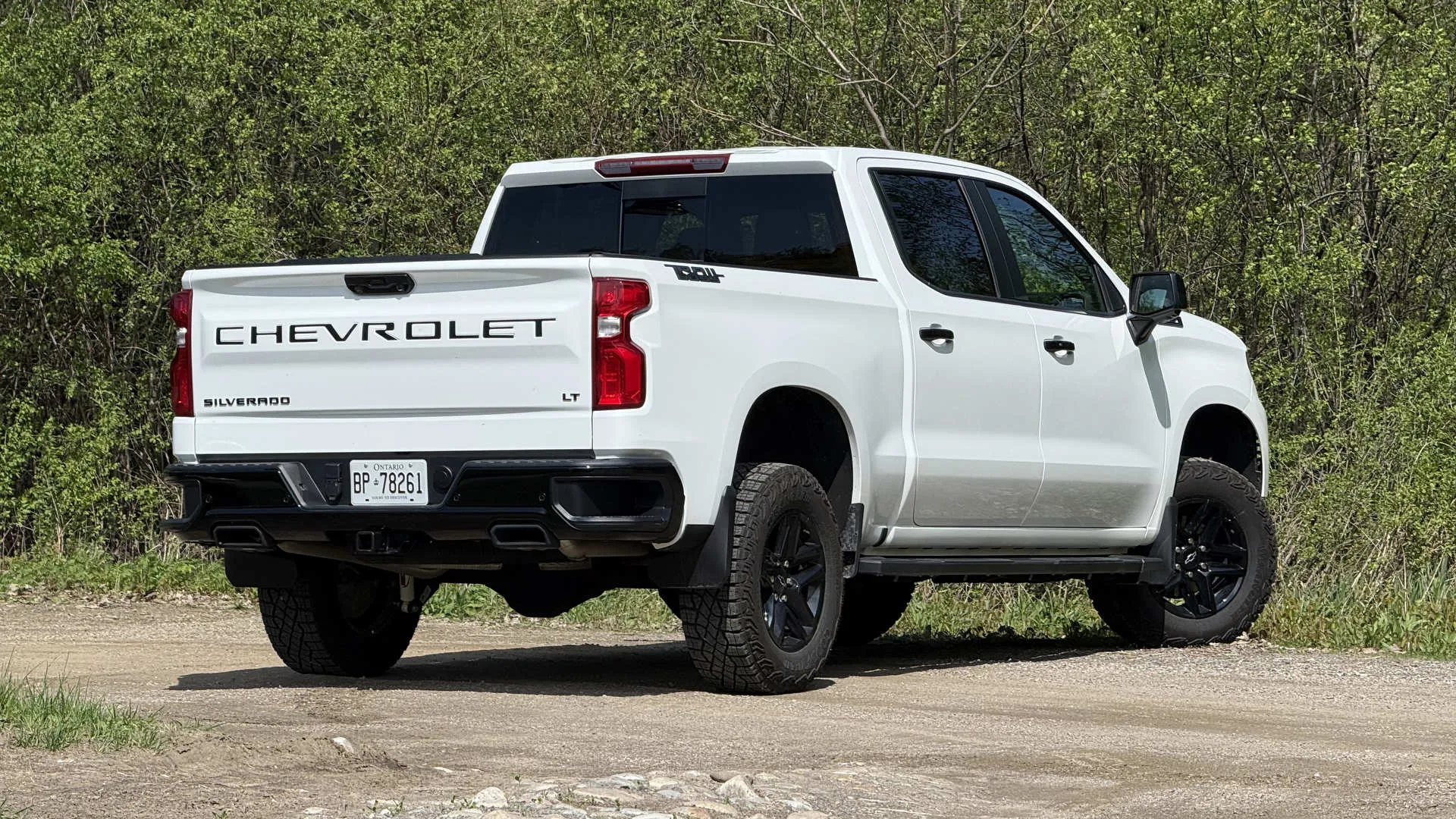 Rear view of a white Chevy Silverado LT Trail Boss with black wheels on a gravel road