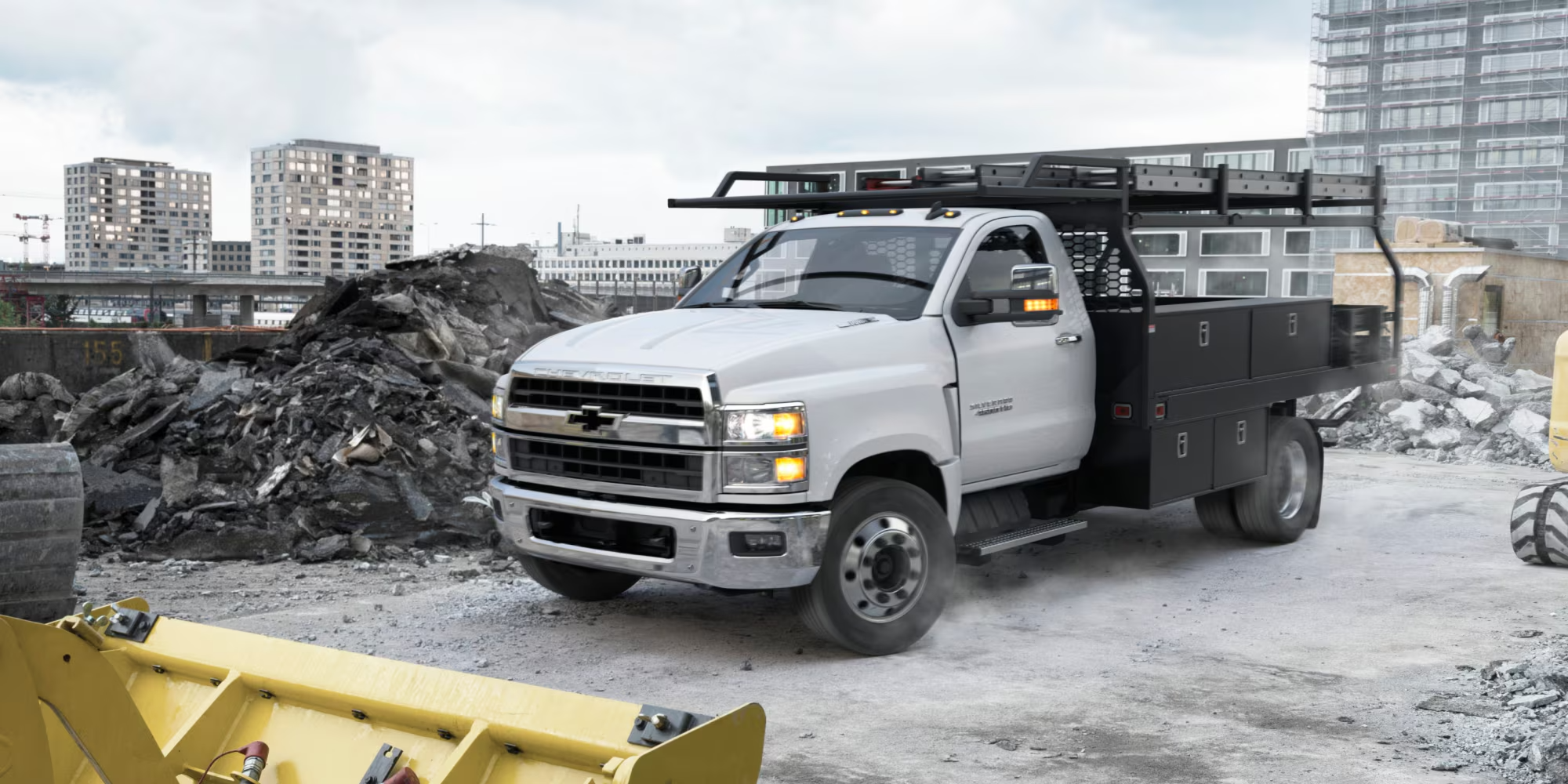 Silver Chevy Silverado medium duty Regular Cab with a contractor body and ladder rack at a demolition site