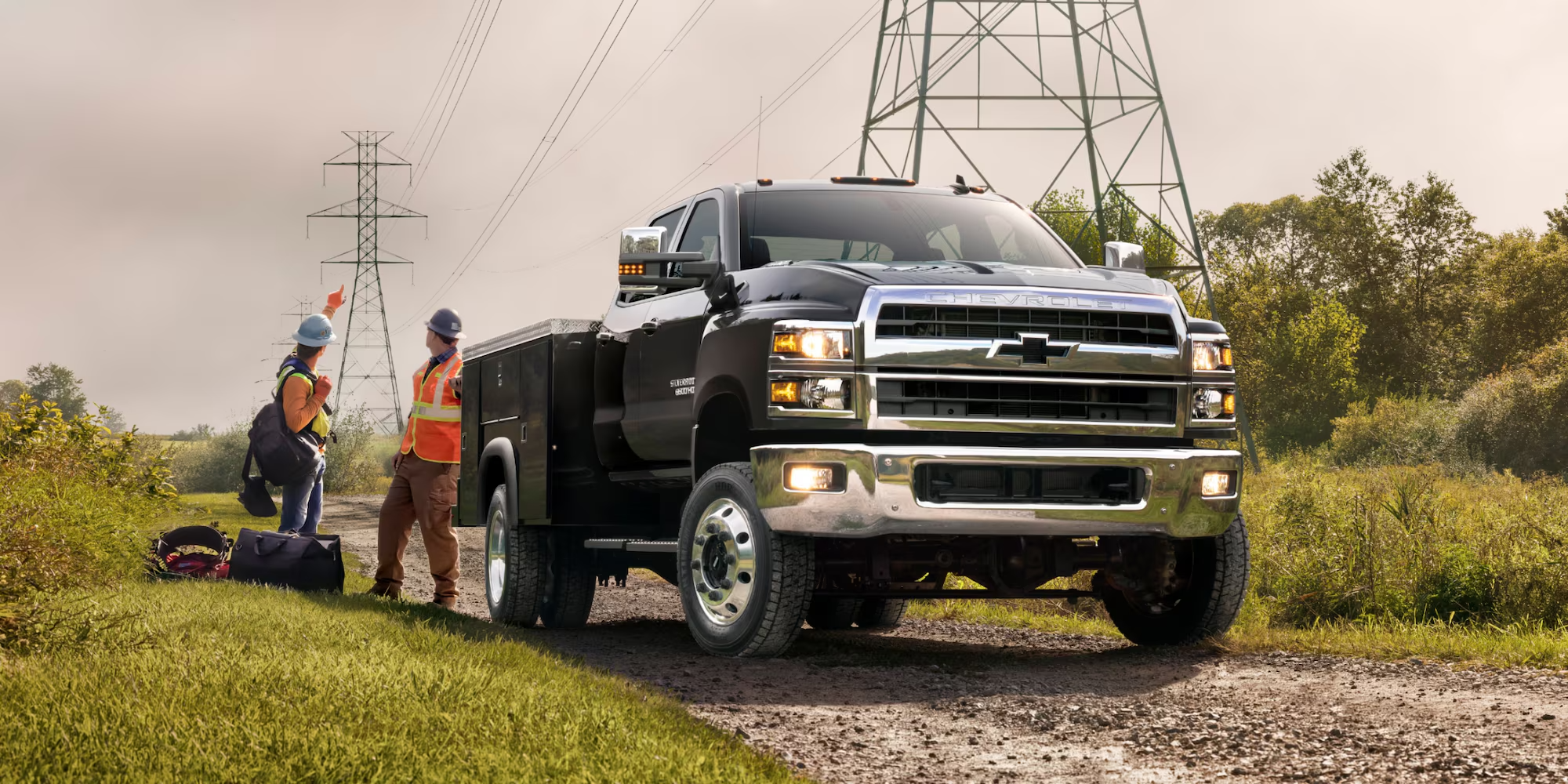 Black Chevy Silverado medium duty chassis cab with a service body and utility crew near power lines
