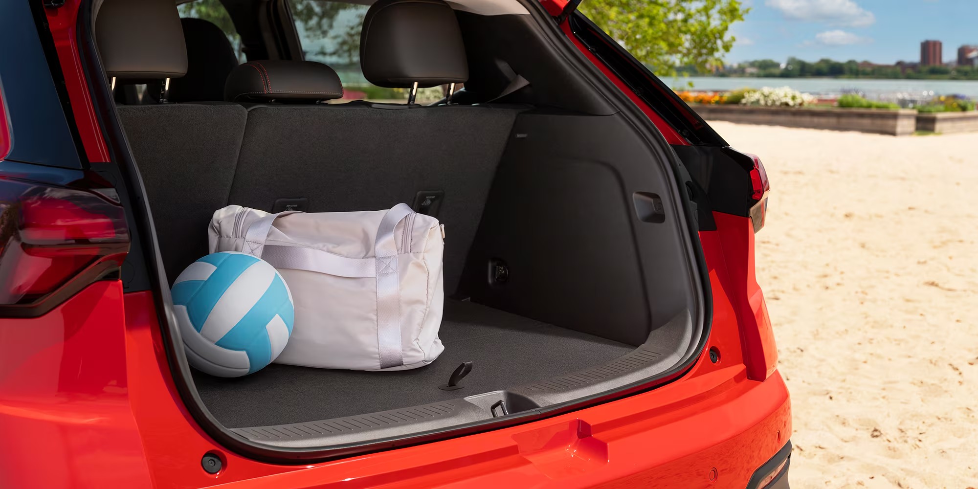 Rear cargo area of a red Chevy Bolt holding a tote bag and volleyball at the beach