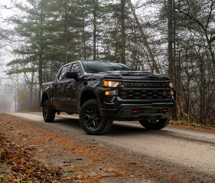 Black Chevy Silverado Custom Trail Boss on a misty forest gravel road covered in fall leaves