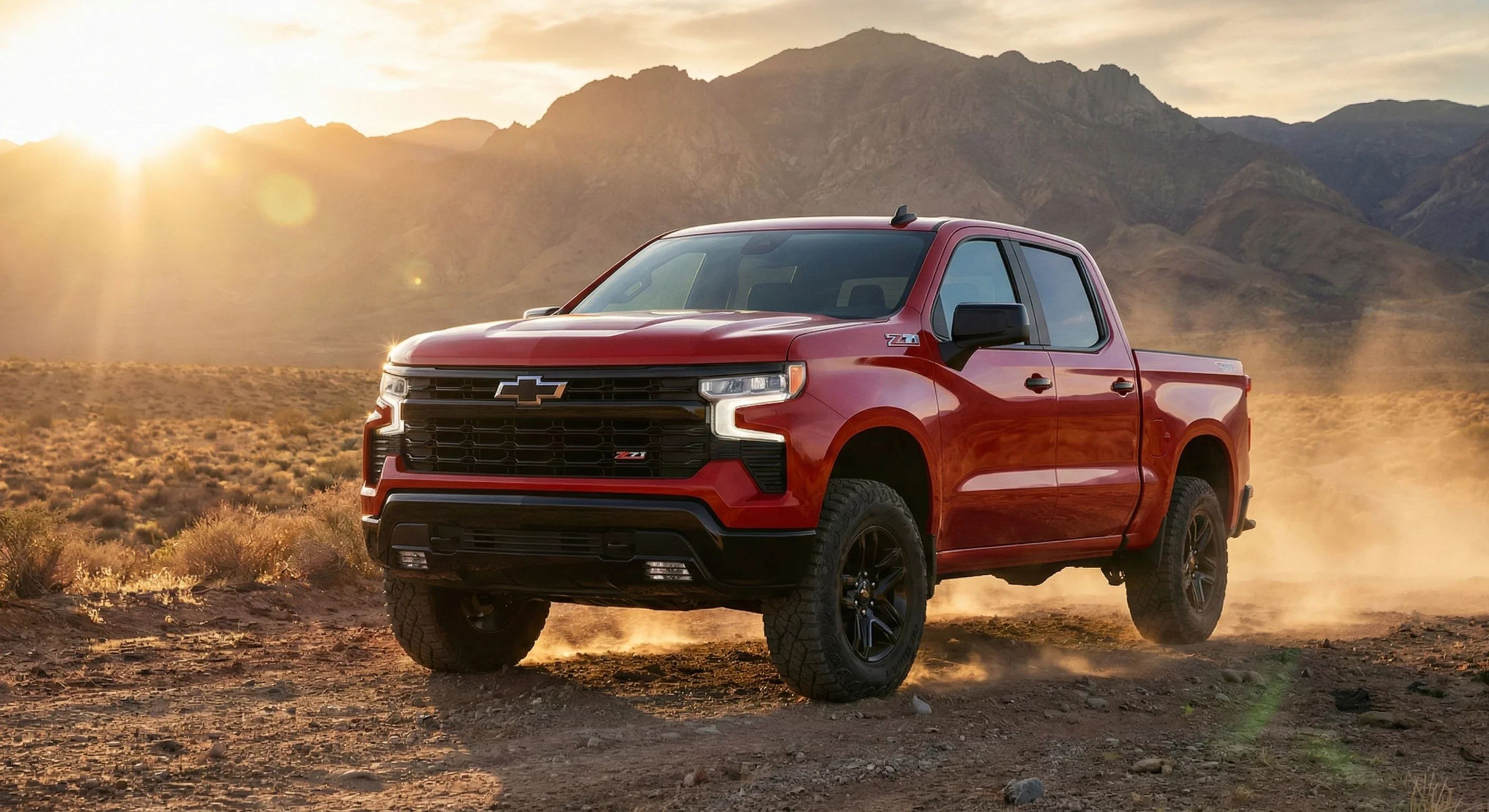 Red Chevy Silverado Trail Boss kicking up dust on a desert trail at sunset below mountains