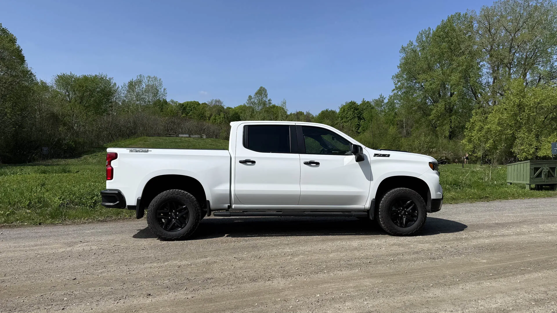 Side profile of a white Chevy Silverado Trail Boss showing its lifted stance and black wheels on a gravel road