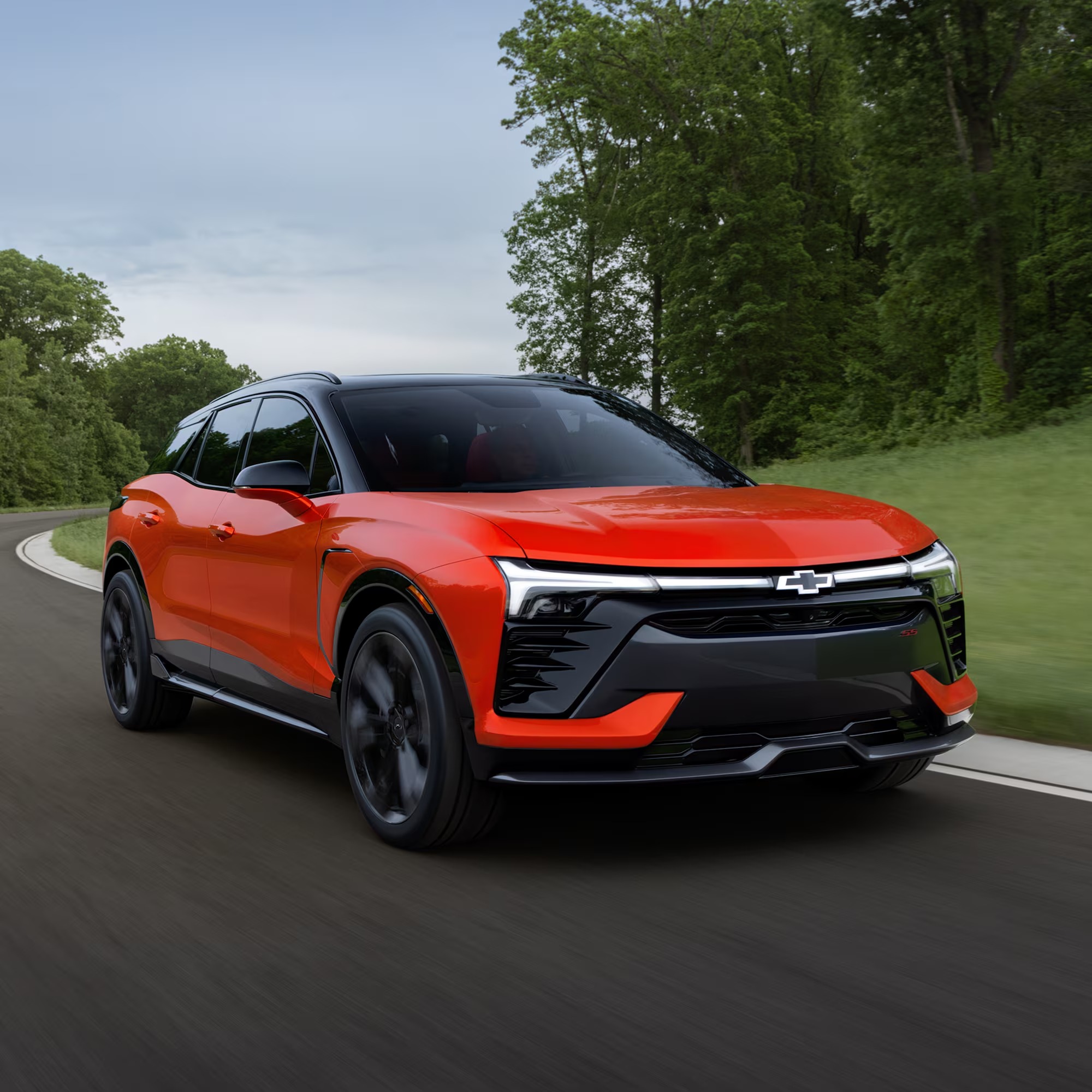 Red Chevy Blazer EV with illuminated front light bar driving on a tree-lined road