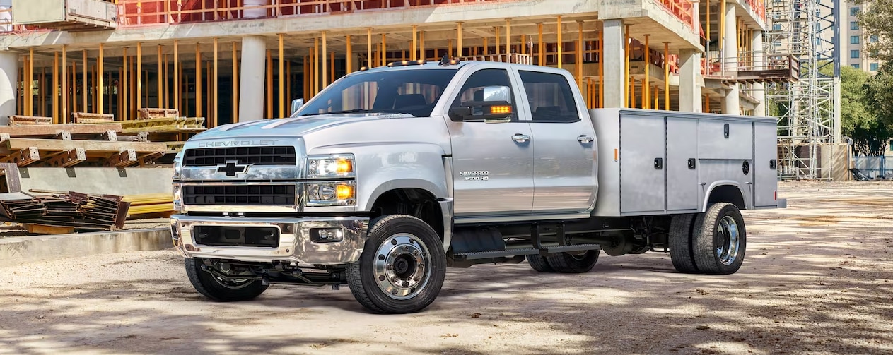 A silver 2023 Chevy Silverado Work Truck with custom tool boxes installed on the back is parked at a construction site.