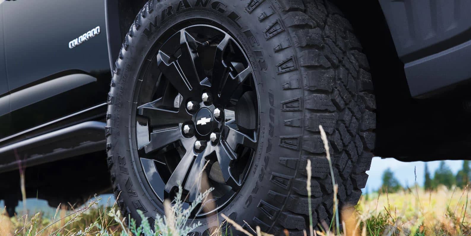 The tire of a black 2023 Chevy Colorado pickup truck parked in the grass