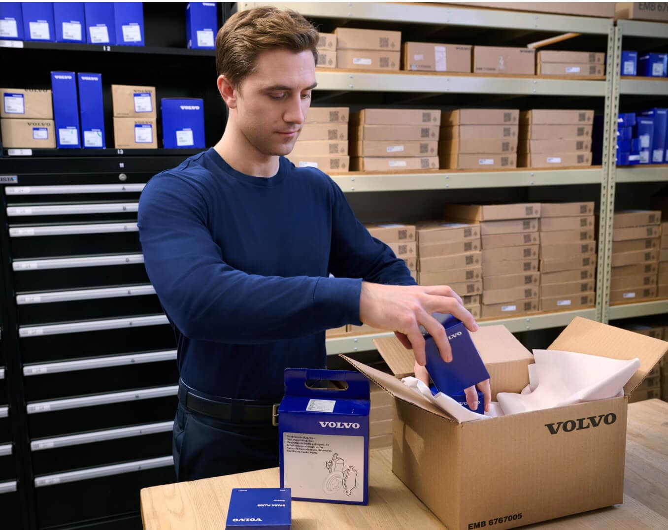 Front view of a parts specialist organizing Volvo auto parts boxes in a service department.