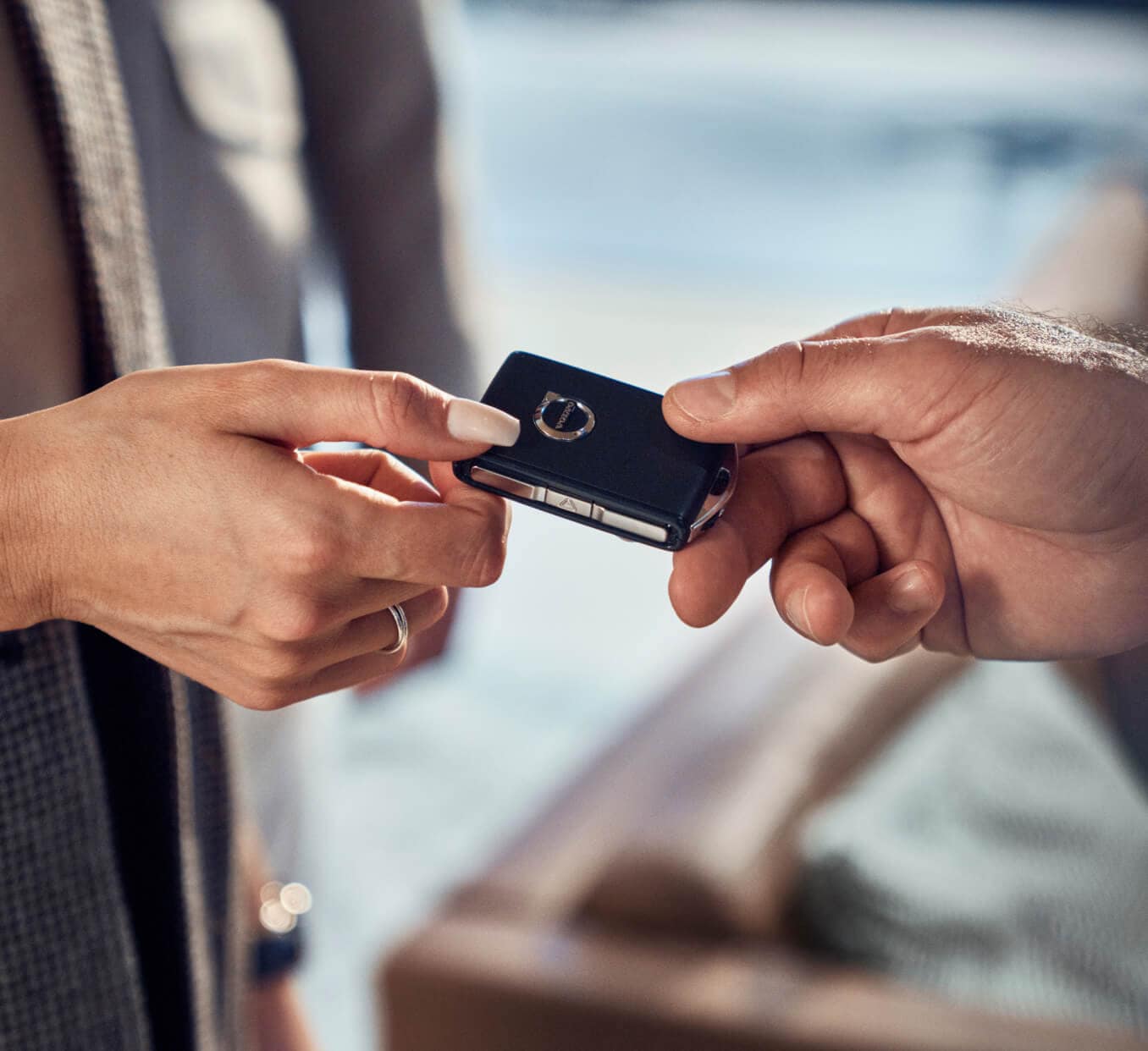 Close-up view of a dealership employee handing a black Volvo key fob to a customer.