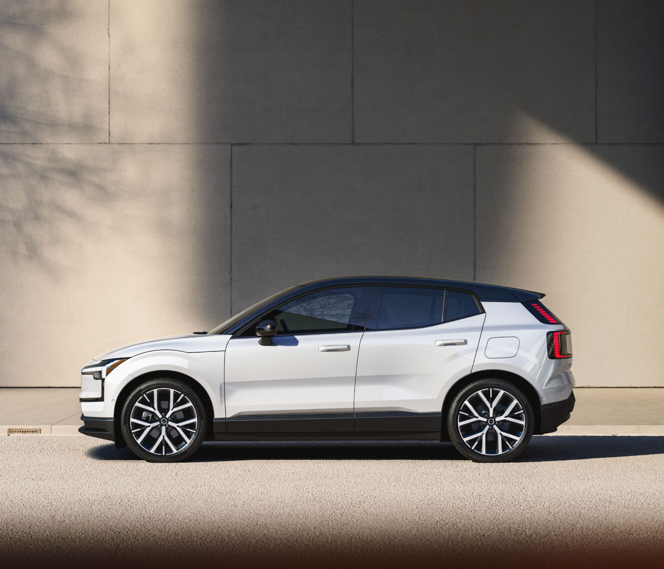 Side profile view of a white 2026 Volvo EX30 parked along a concrete wall.