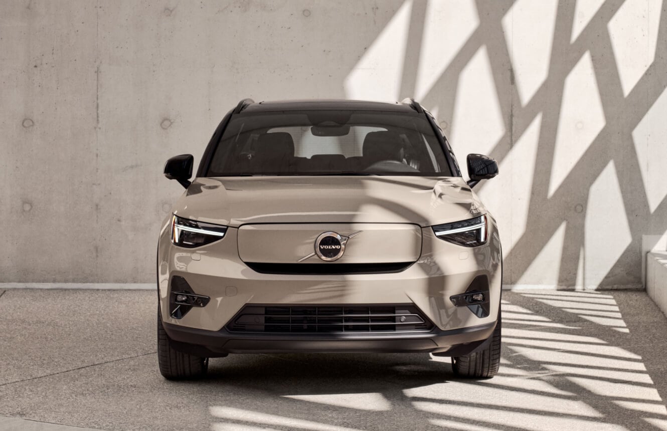 Front view of a beige 2026 Volvo EX40 under geometric shadows against a concrete wall.
