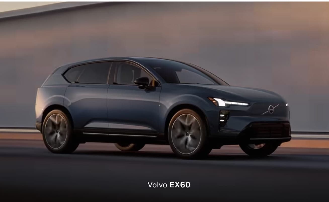 A sleek, modern 2026 Volvo EX60 SUV in Denim Blue color, driving on a road, highlighted by the soft glow of sunset. Its design is elegant and dynamic.