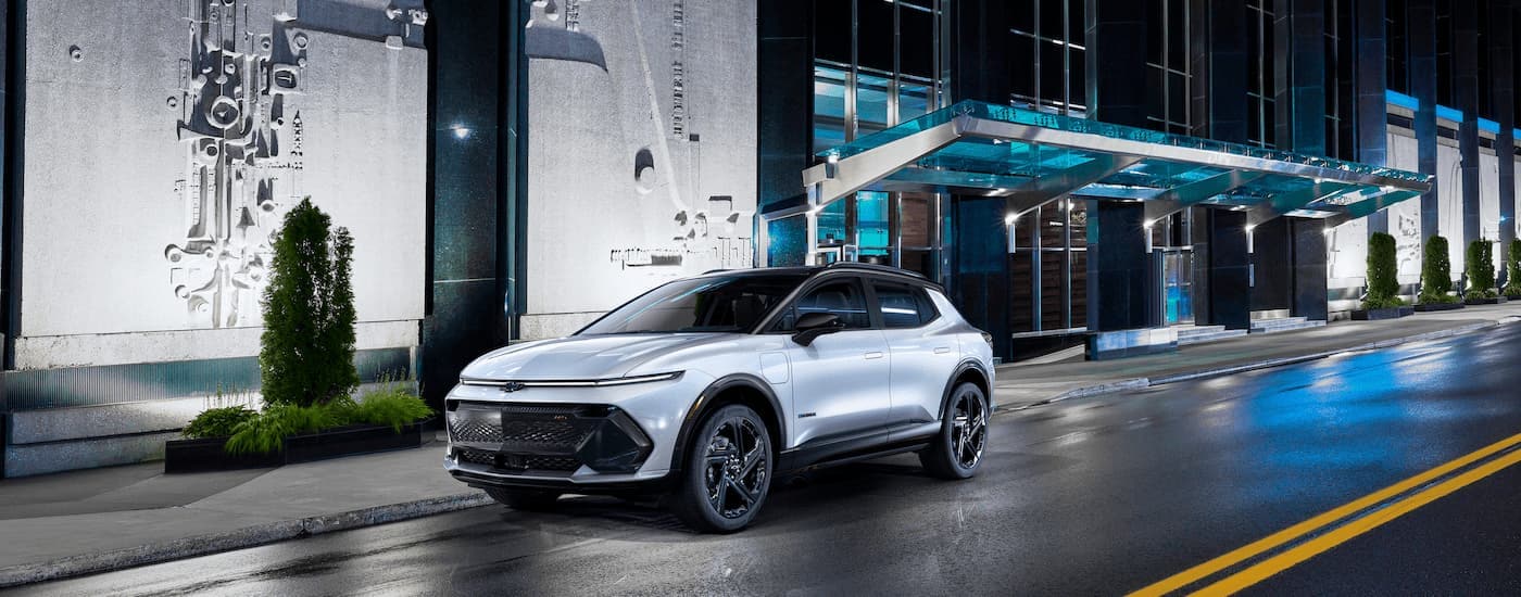 A white 2024 Chevy Equinox EV 3RS is shown driving on a city street at night.