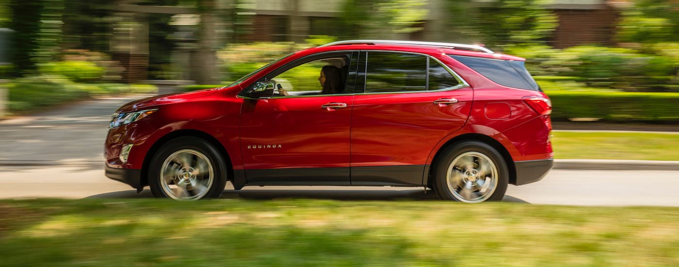A red 2018 Chevy Equinox is shown from the side driving on a tree-lined road near Columbus, OH.