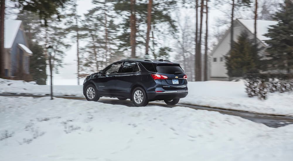 A dark blue 2018 Chevy Equinox is shown driving on a snowy street.