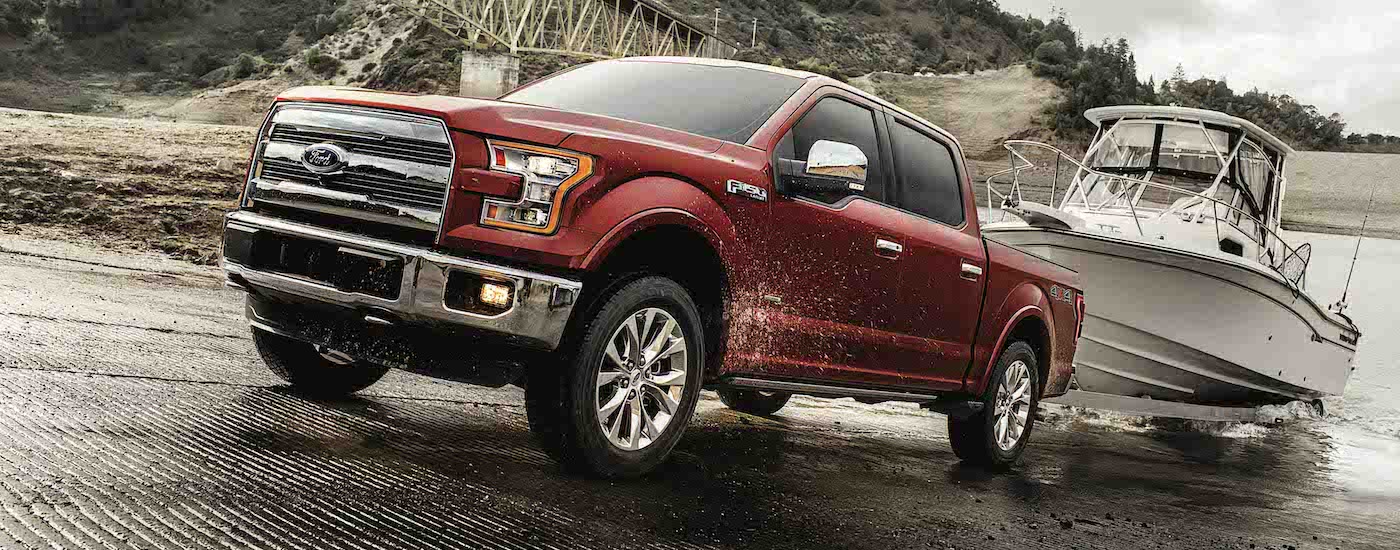 A red 2017 Ford F-150 is shown towing a white fishing boat out of a lake.
