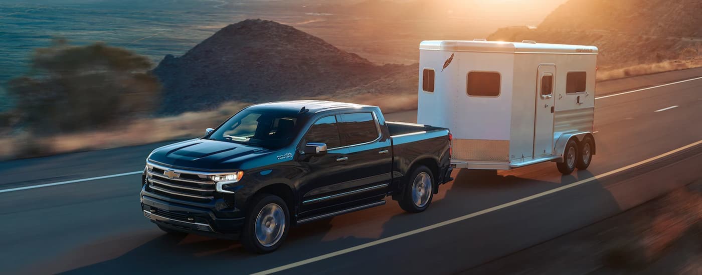 A black 2022 Chevy Silverado 1500 High Country for sale is shown towing a trailer on an open road.