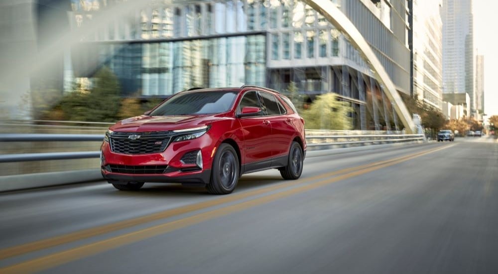 A red 2023 Chevy Equinox RS is shown driving on a city street after leaving a Chevy dealer near you.