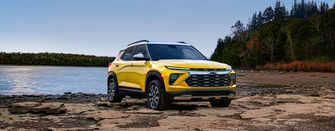 A yellow 2024 Chevy Trailblazer is shown parked on rock near a lake.