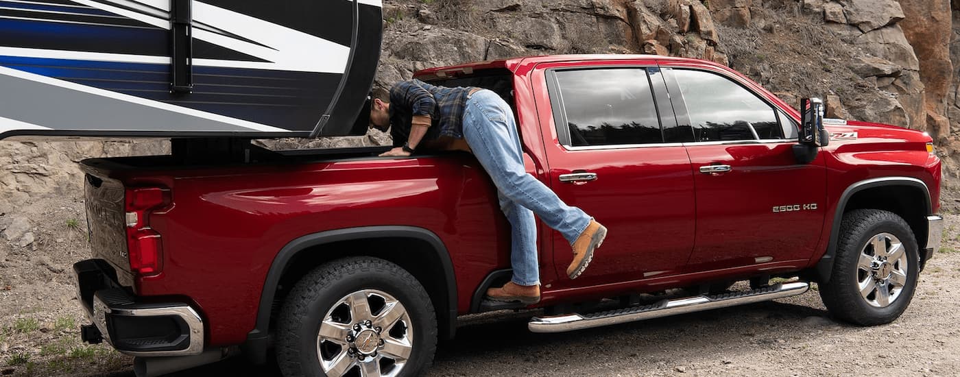 A man is shown leaning into the bed of a red 2023 Chevy Silverado 2500HD Z71 towing camper trailer.