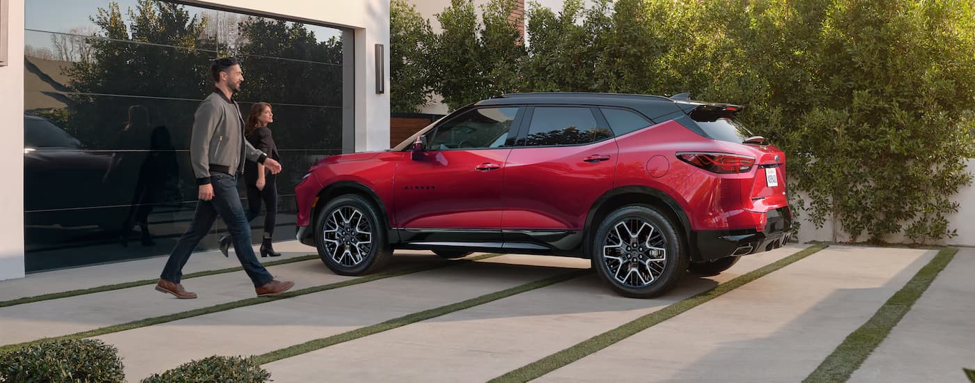 A red 2025 Chevy Blazer RS is parked in a driveway as two people walk towards it.