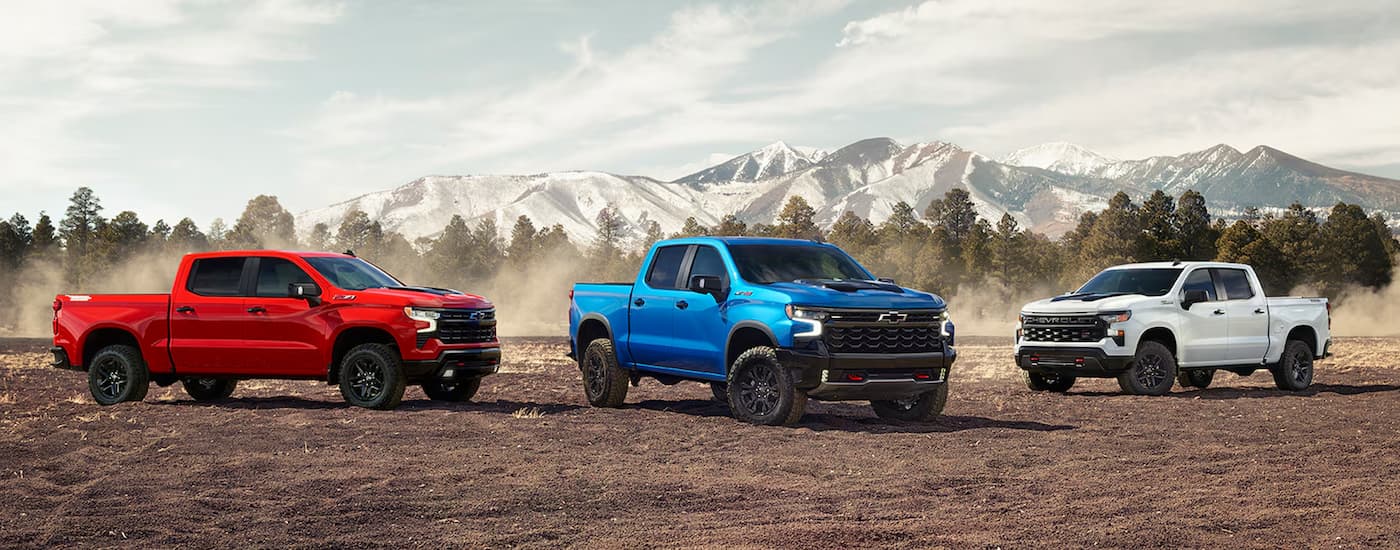 A group of three 2024 Chevy Silverado 1500s are shown parked on dirt.