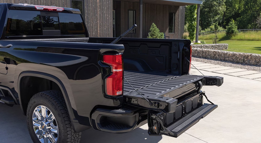 The open Multi-Flex Tailgate of a black 2025 Chevy Silverado 2500 HD parked in a driveway.