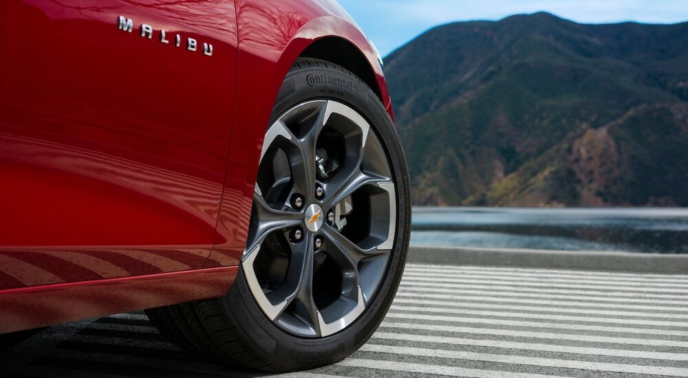 A close-up shows the front wheel of a red 2024 Chevy Malibu RS.