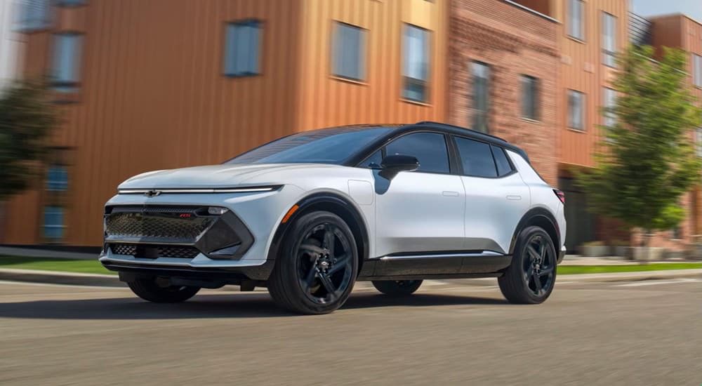 A white 2025 Chevy Equinox EV RS is driving on a city street.