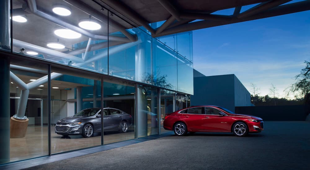A silver and a red 2024 Chevy Malibu for sale are shown on opposing sides of glass.