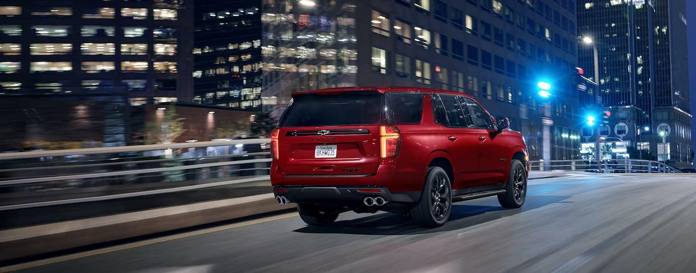 A red 2024 Chevy Tahoe RST is shown from a rear angle driving on a city street.